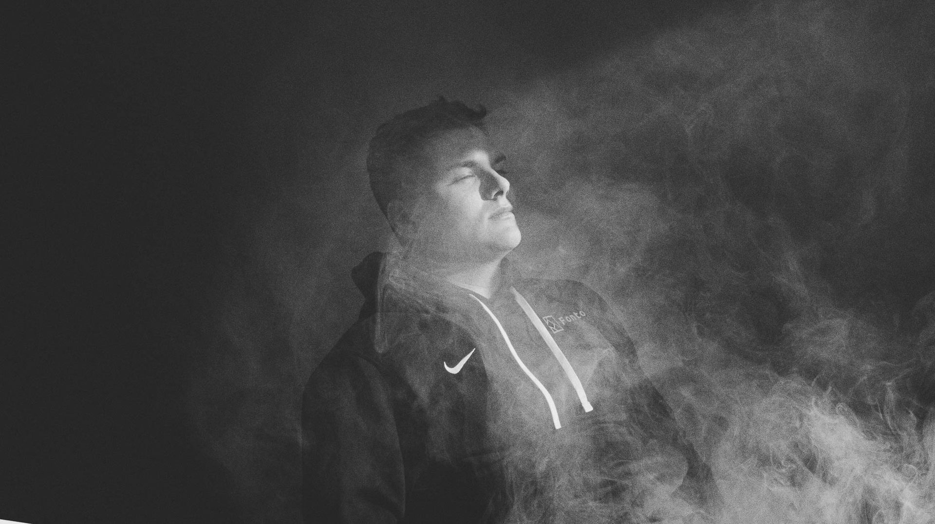 a black white image of a guy sitting in the sun inside with smoke surrounding